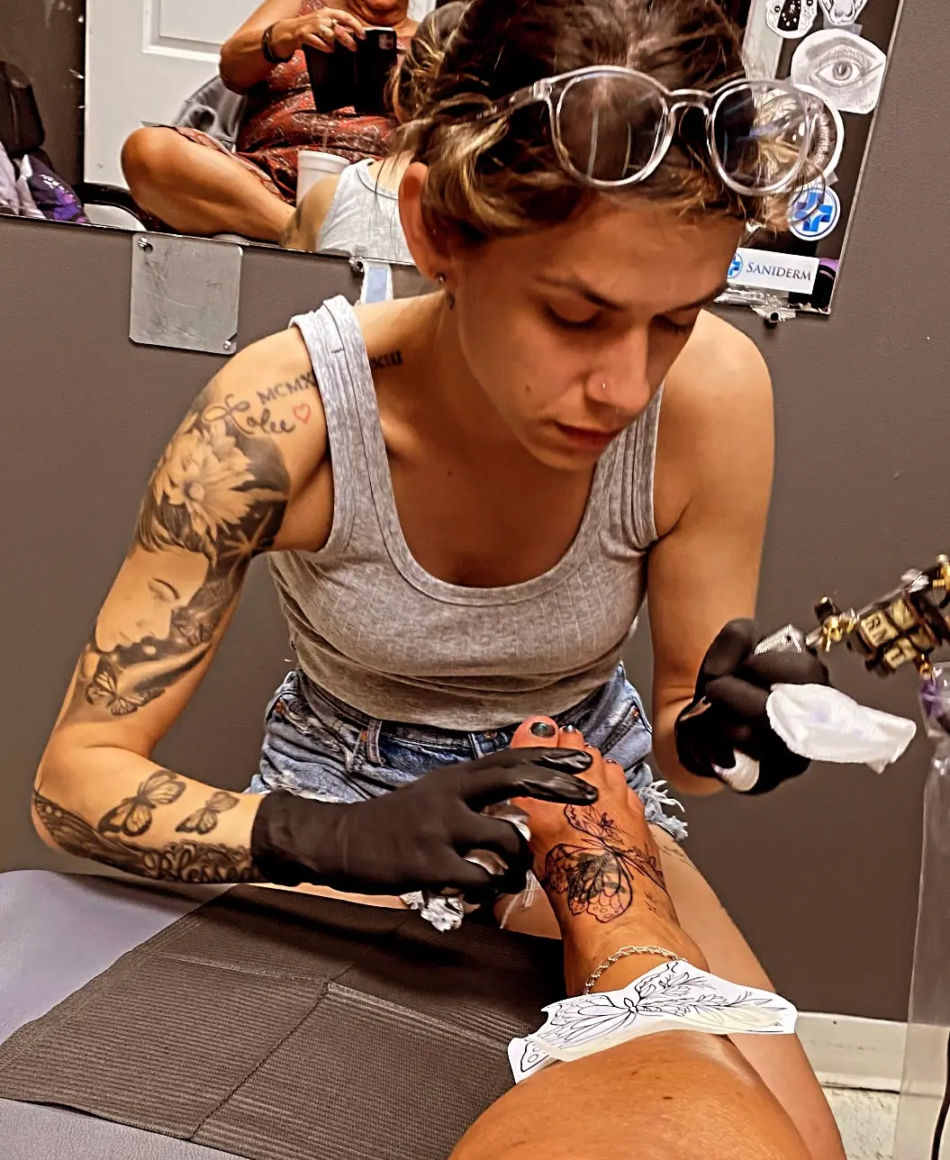 Carly tattooing a butterfly piece on a client's foot at Bewitched Tattoo