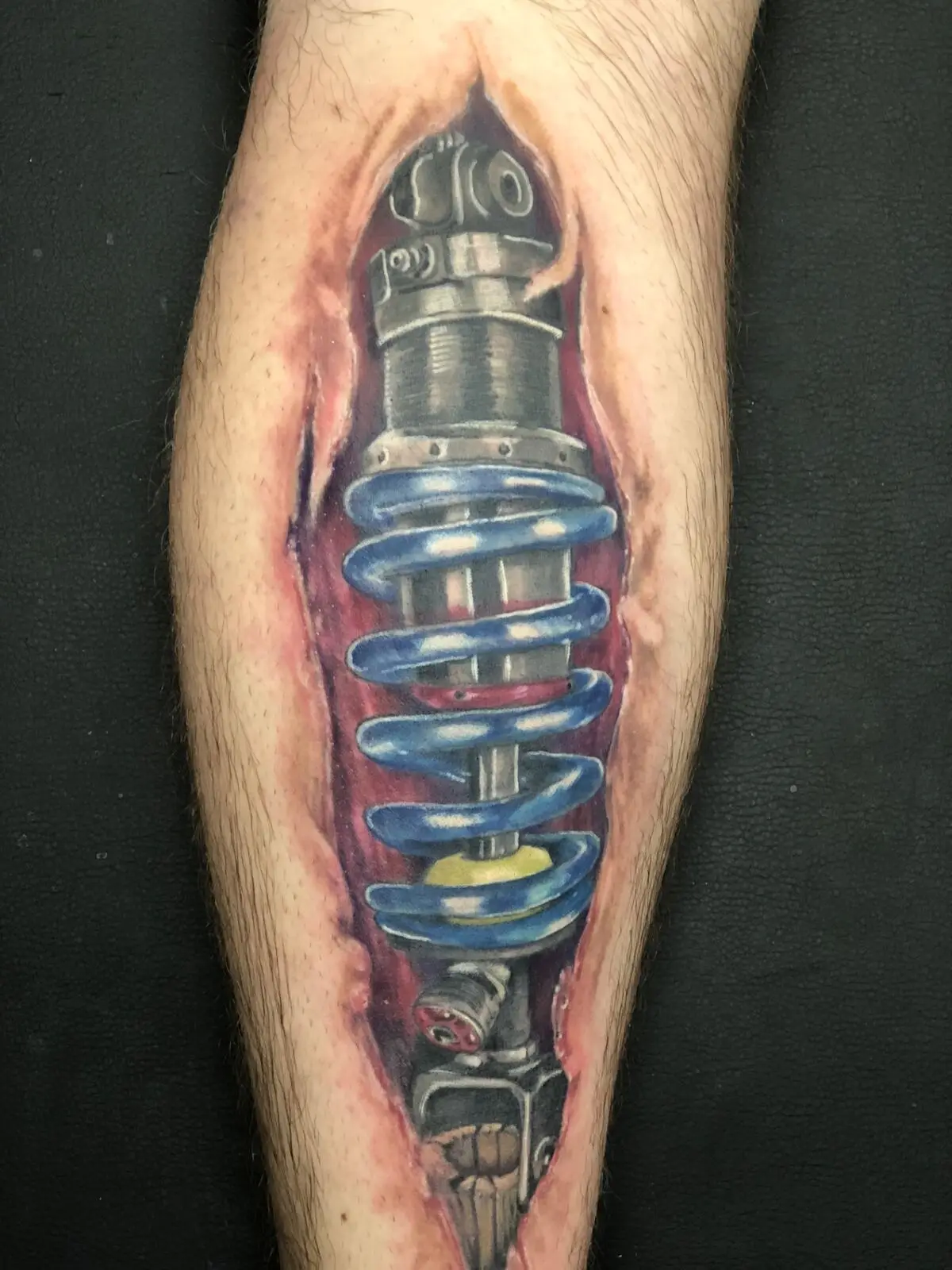 Hyper-realistic biomechanical coil-over shock absorber torn-skin tattoo on calf