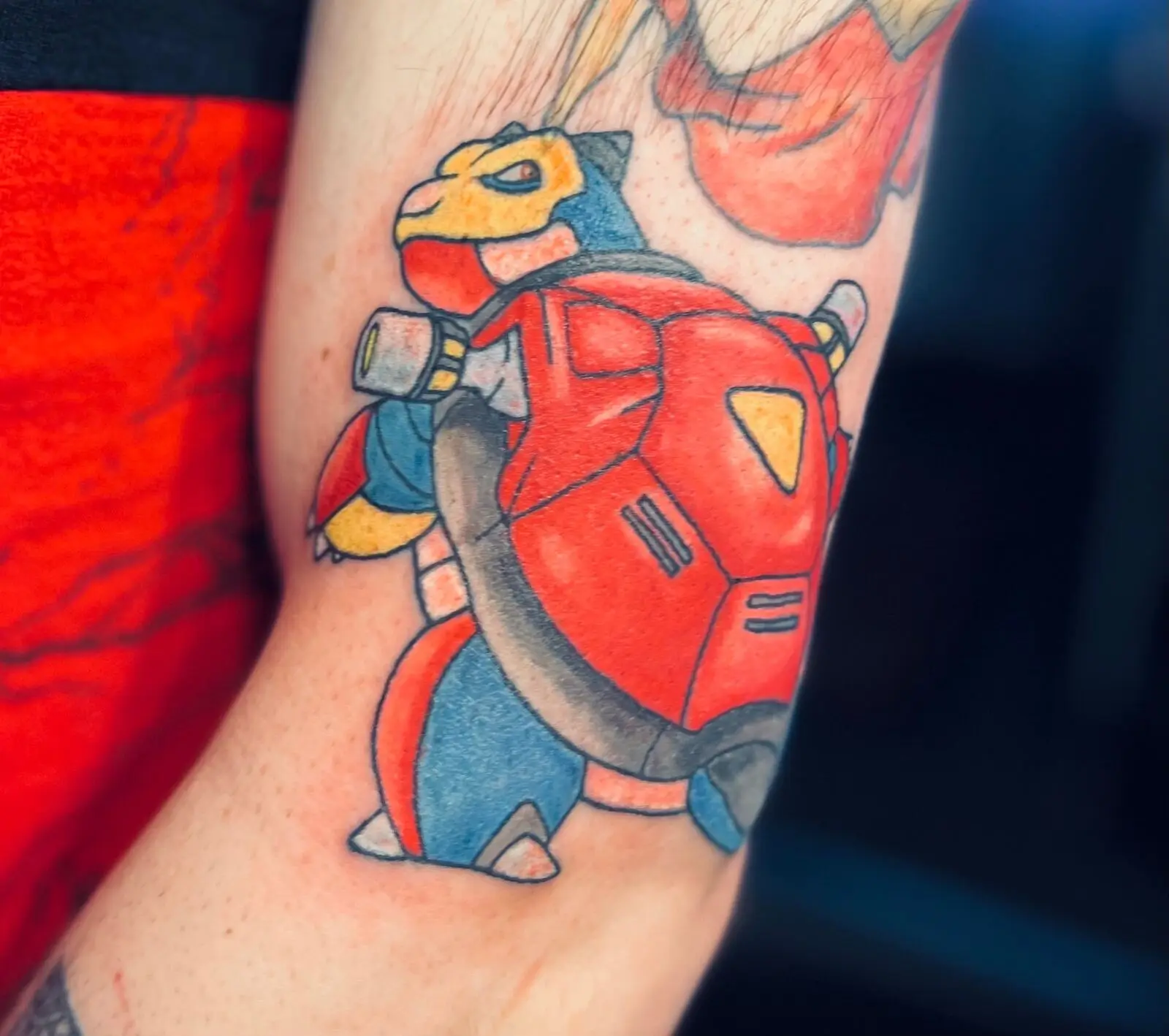 Bright color tattoo of a cartoon Blastoise character wearing red armor on the lower leg