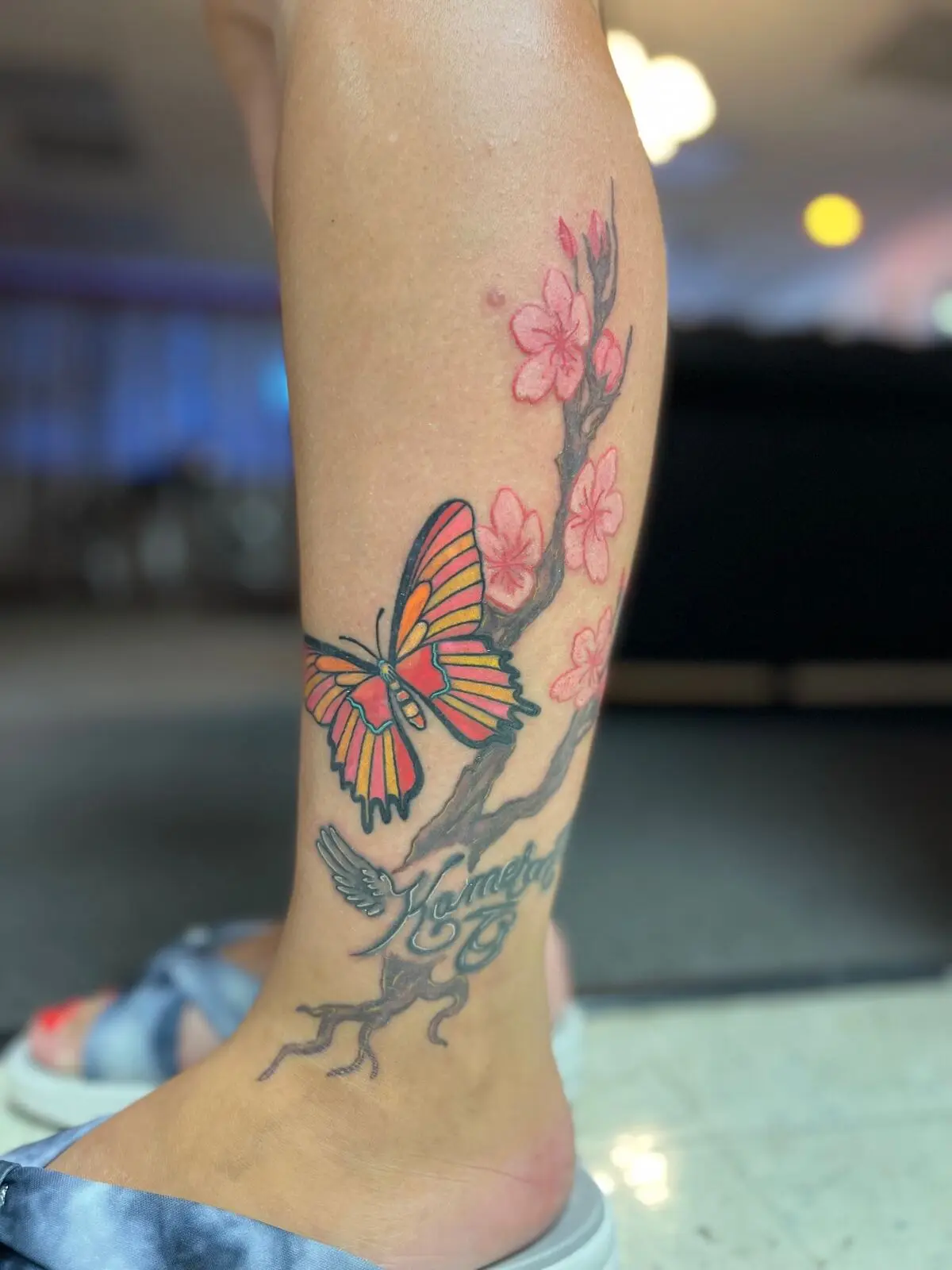 Color calf tattoo of a red and yellow stained glass butterfly on a pink cherry blossom branch