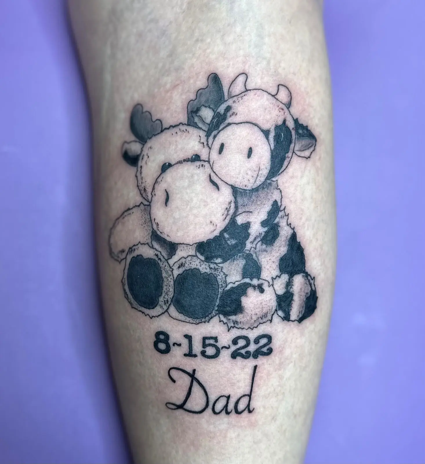 Black and grey cow plushie pair memorial tattoo with date 8-15-22 and Dad script on calf