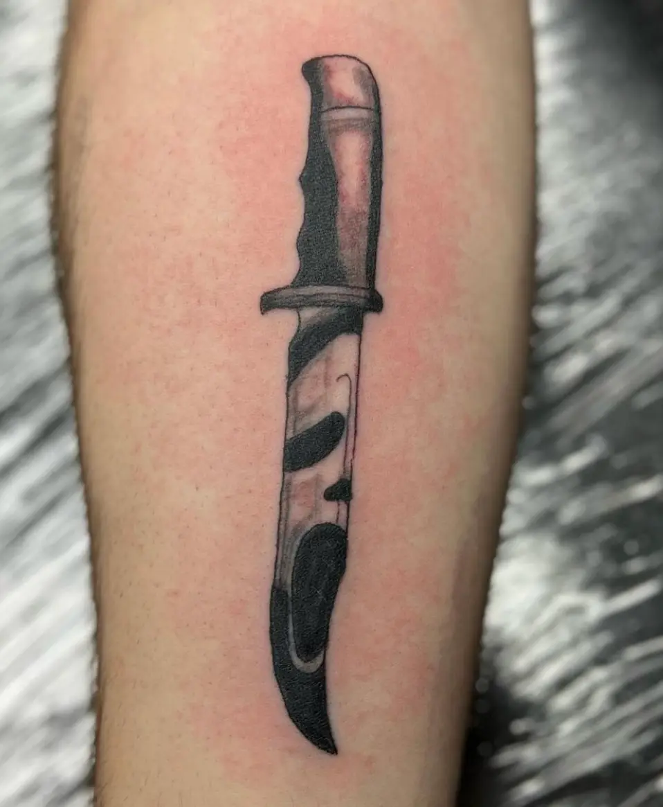 Realistic black and grey dagger tattoo with reflective blade detail on the forearm