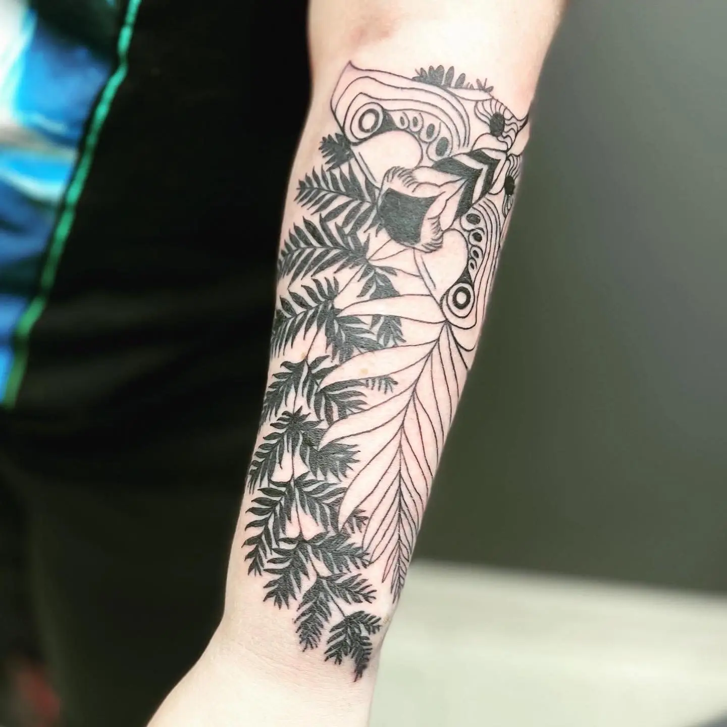 Botanical black and grey forearm tattoo with detailed ferns flowing into an abstract linework design
