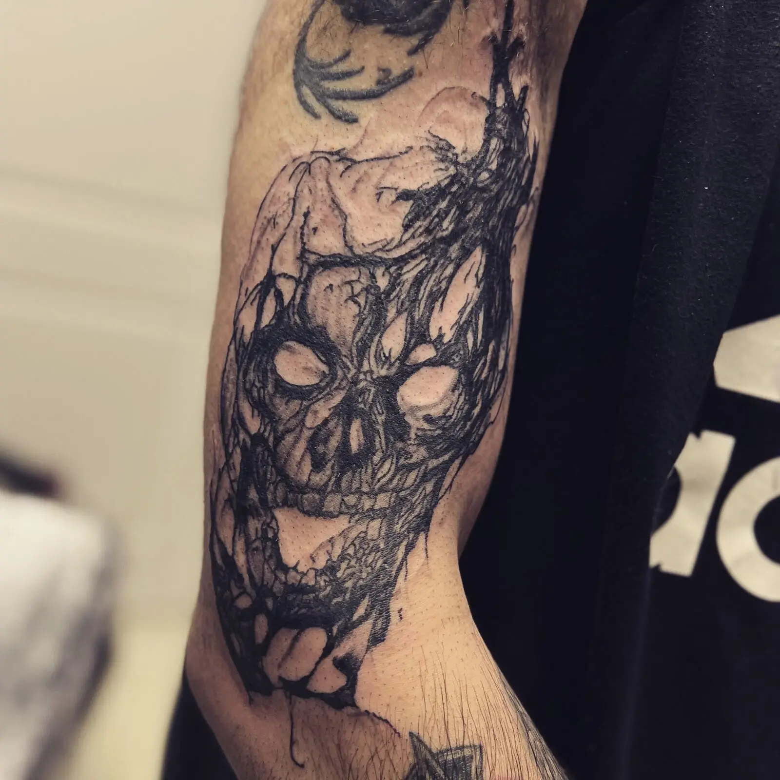 Black and grey illustrative skull tattoo with fractured, sketch-like details running along the forearm