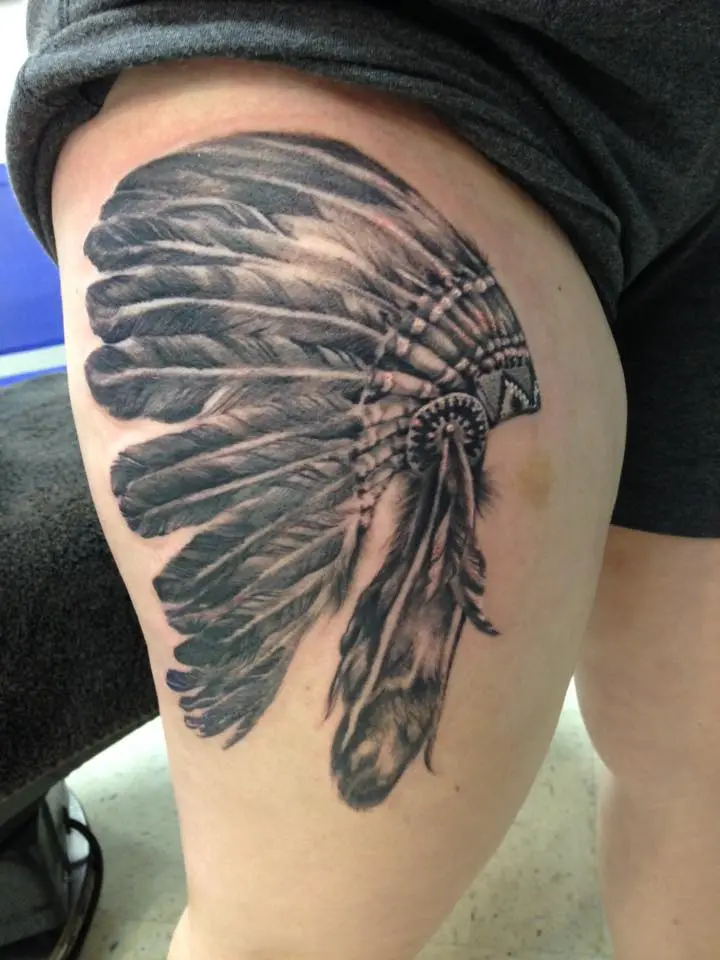 Black and grey realism thigh tattoo of a Native American feathered headdress with detailed beadwork