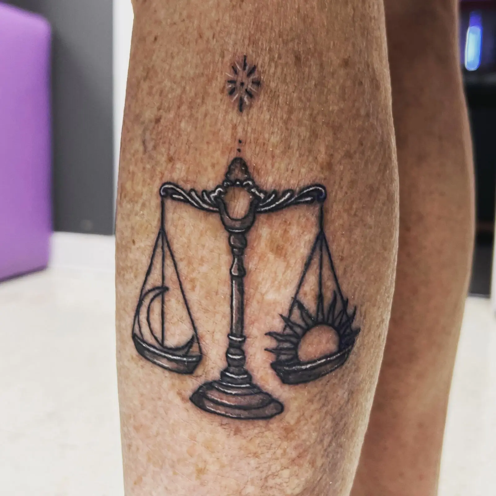 Black and grey Libra scales tattoo with a crescent moon on one side and a rising sun on the other