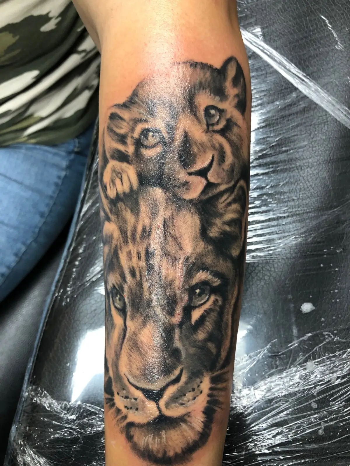Black and grey lion face tattoo stretched vertically down the forearm