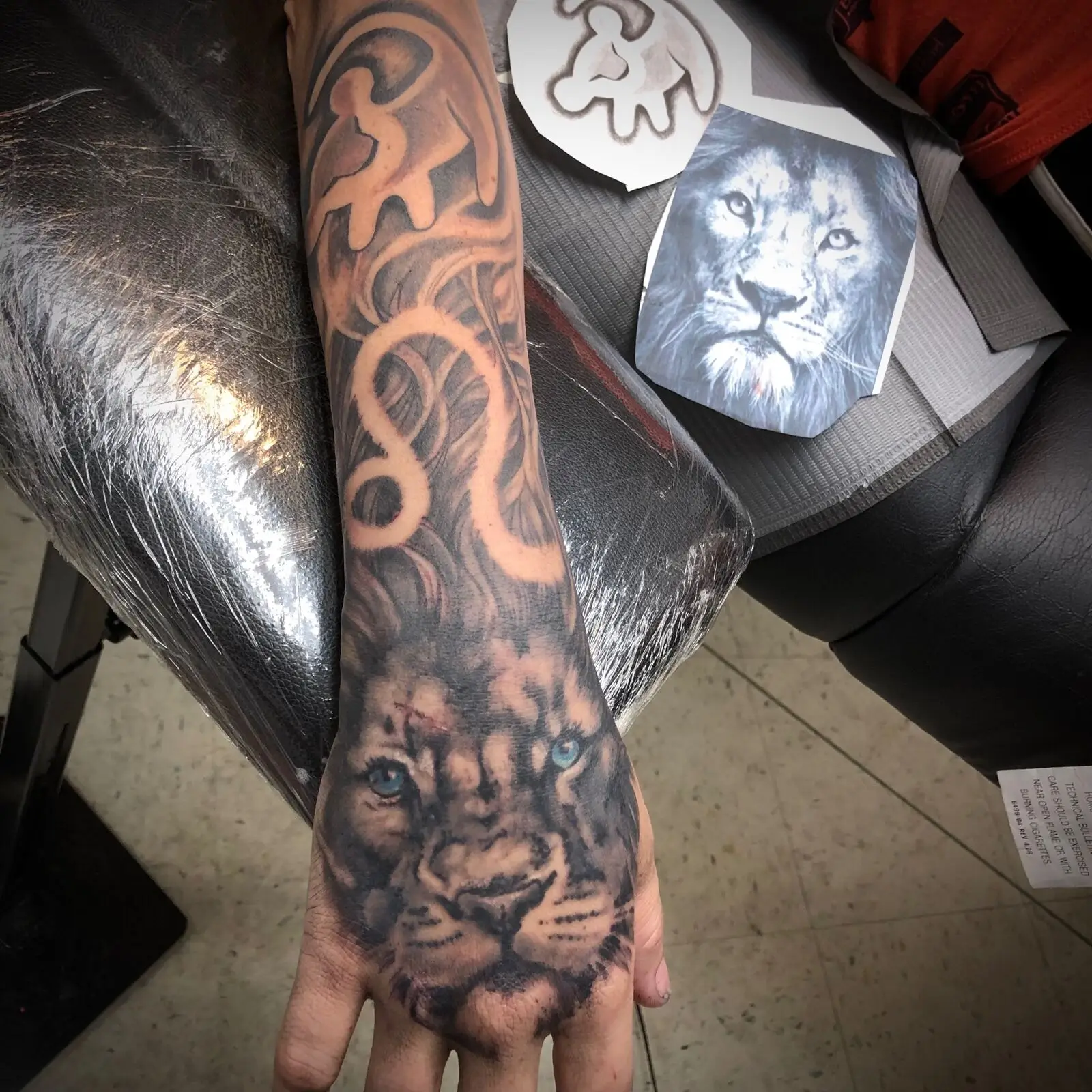 Black and grey lion hand tattoo with blue eyes flowing into forearm sleeve