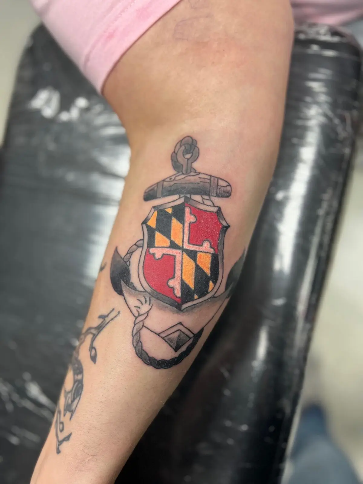 Traditional color tattoo of an anchor wrapped around a Maryland flag shield crest, by Carly