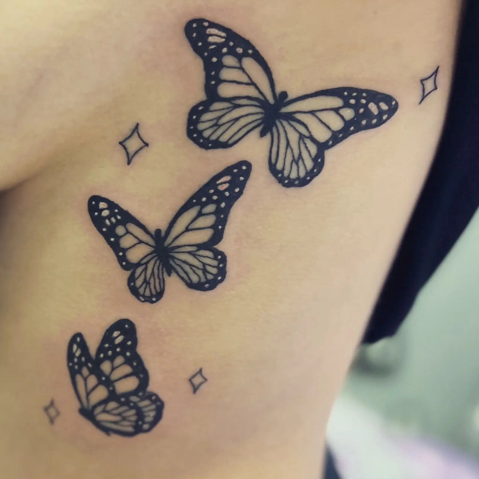 Fine line blackwork butterfly tattoo cluster with small sparkle stars on the upper arm