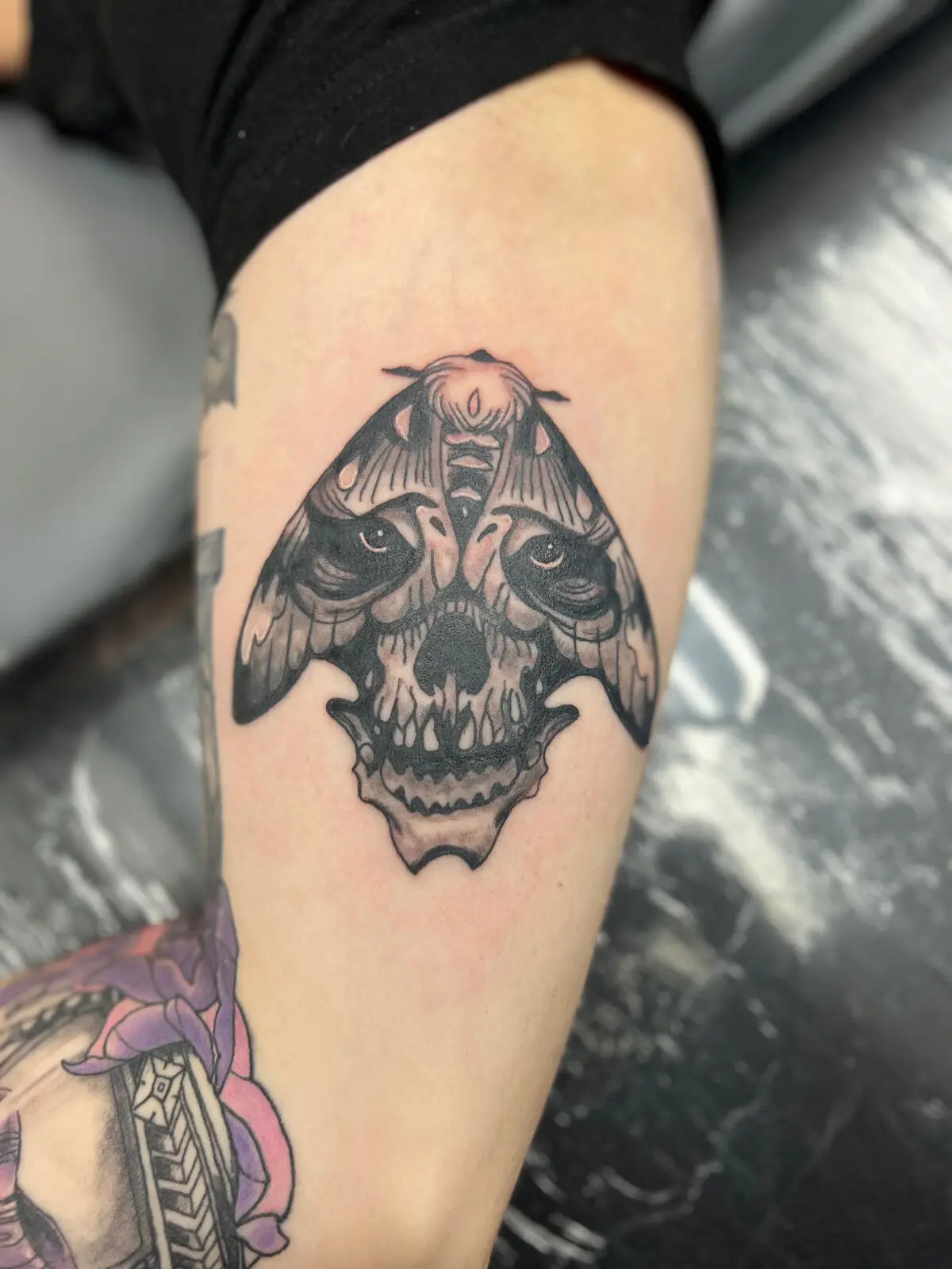 Black and grey moth tattoo merged with a skull face centered on the calf with smooth gradient shading