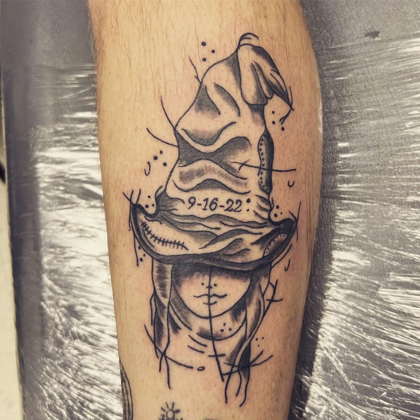 Black and grey illustrative calf tattoo of Oogie Boogie above Sally from Nightmare Before Christmas with memorial date 9-16-22, by Carly