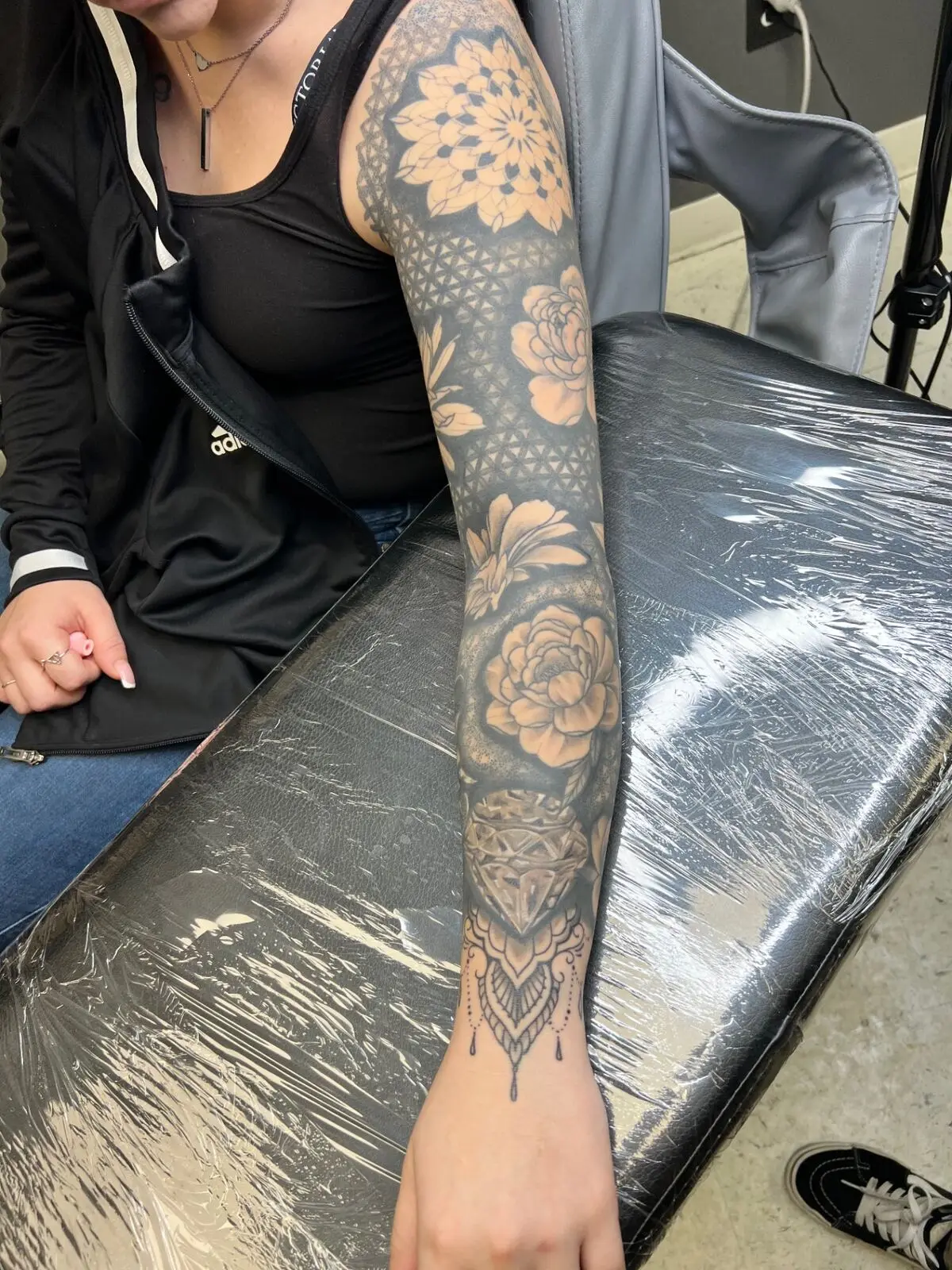 Full black and grey ornamental sleeve combining mandalas, sacred geometry, peonies and a diamond with hanging jewelry, by Carly