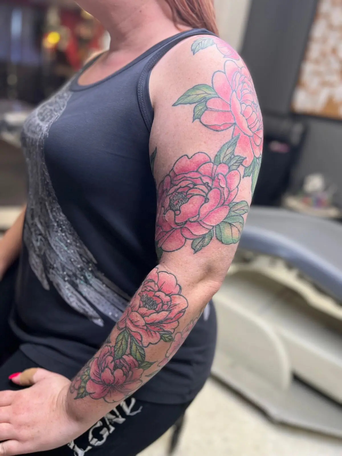 Soft pink watercolor peony half sleeve with green leaves flowing from shoulder to forearm, by Carly