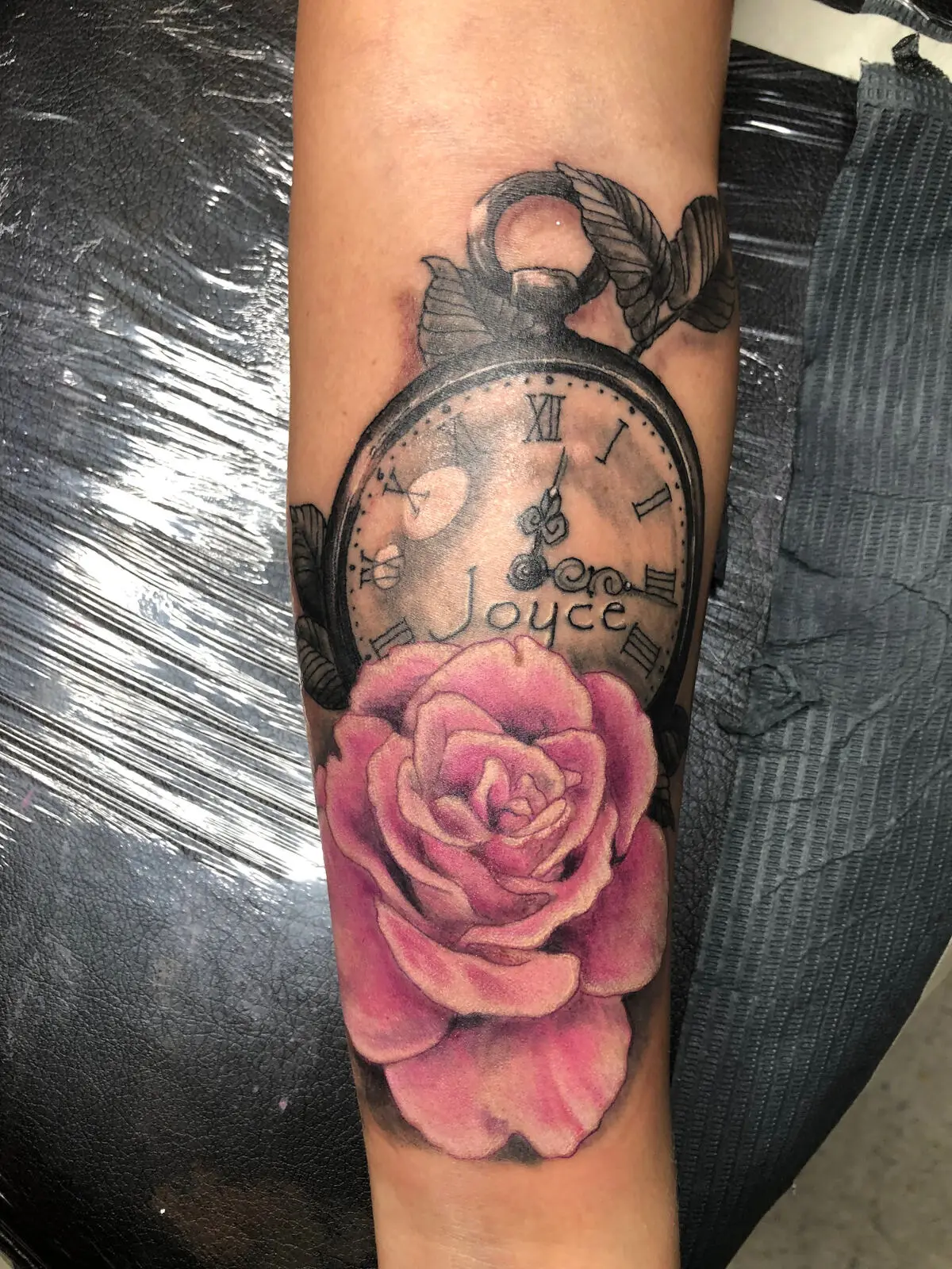 Black and grey pocket watch forearm tattoo engraved Joyce paired with a soft pink realism rose