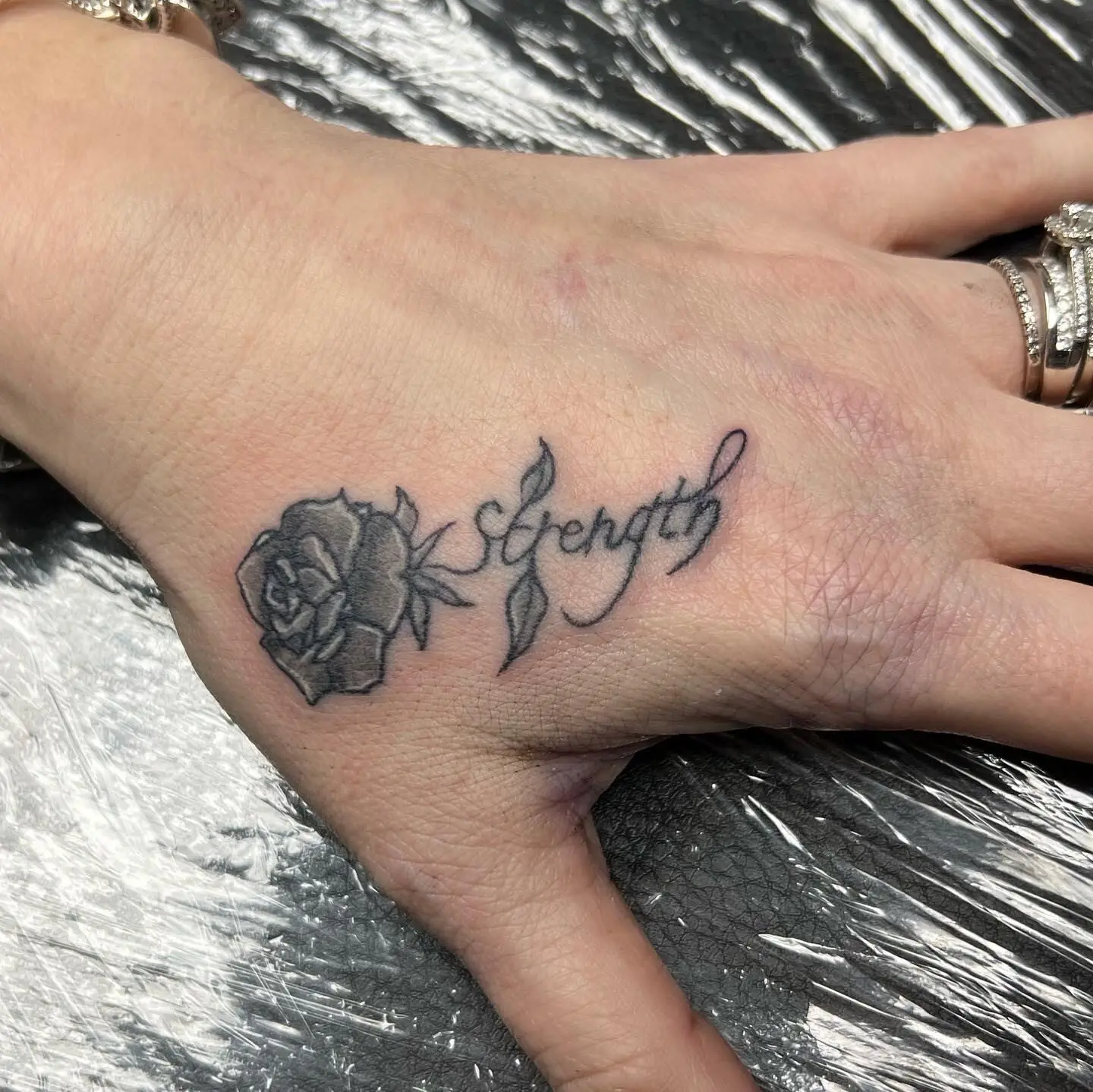 Black and grey hand tattoo with a rose beside script lettering spelling Seraph