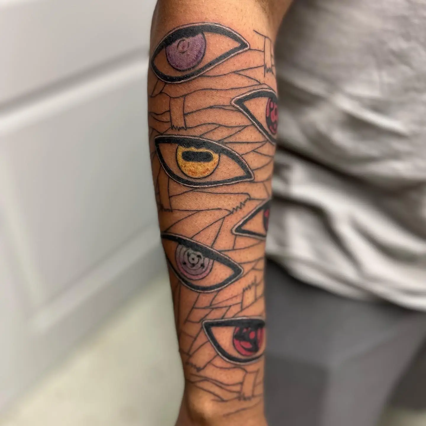 Illustrative forearm tattoo of stacked stylized eyes in purple, gold, and red over geometric linework