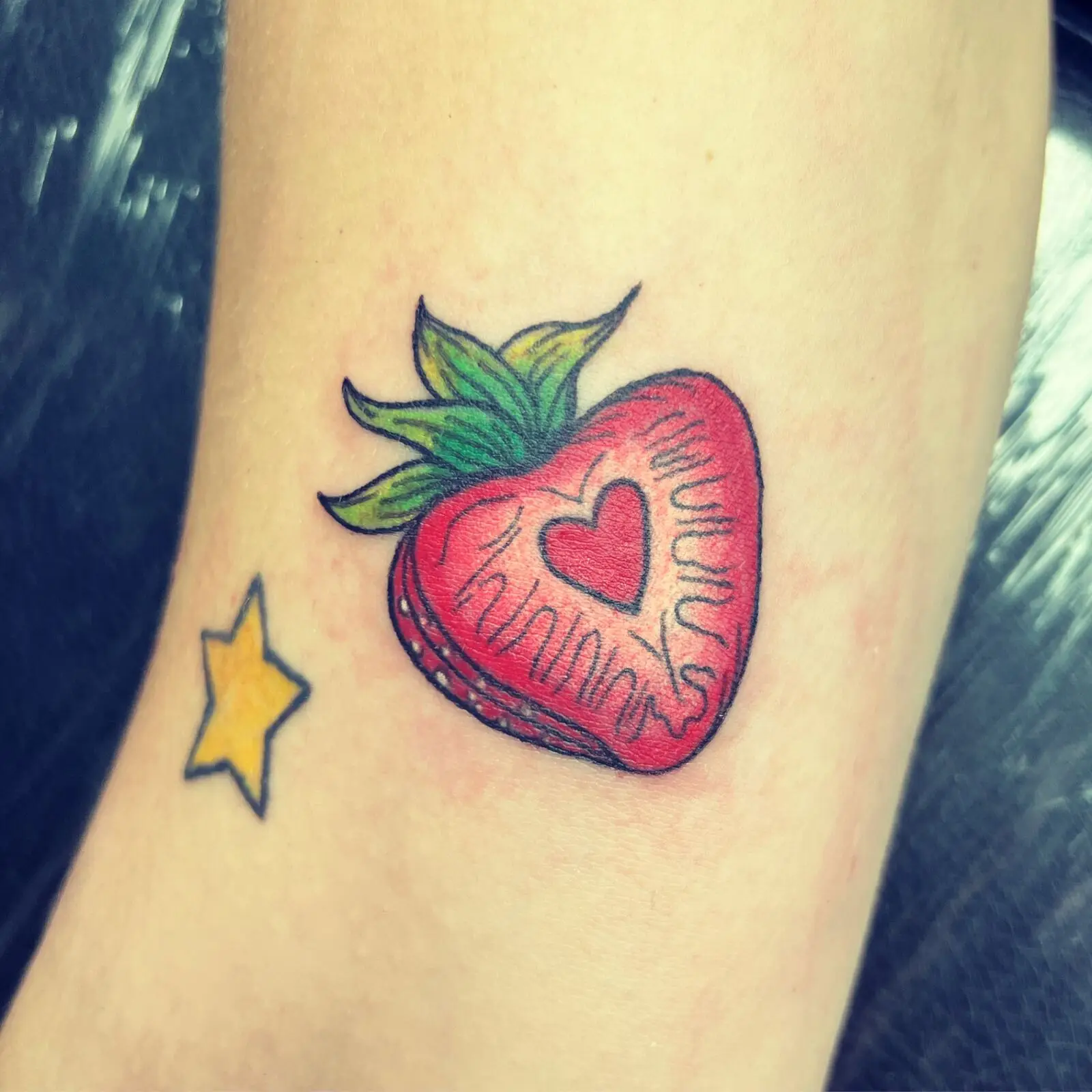 Color tattoo of a sliced strawberry with a heart center alongside a small yellow star on the ankle