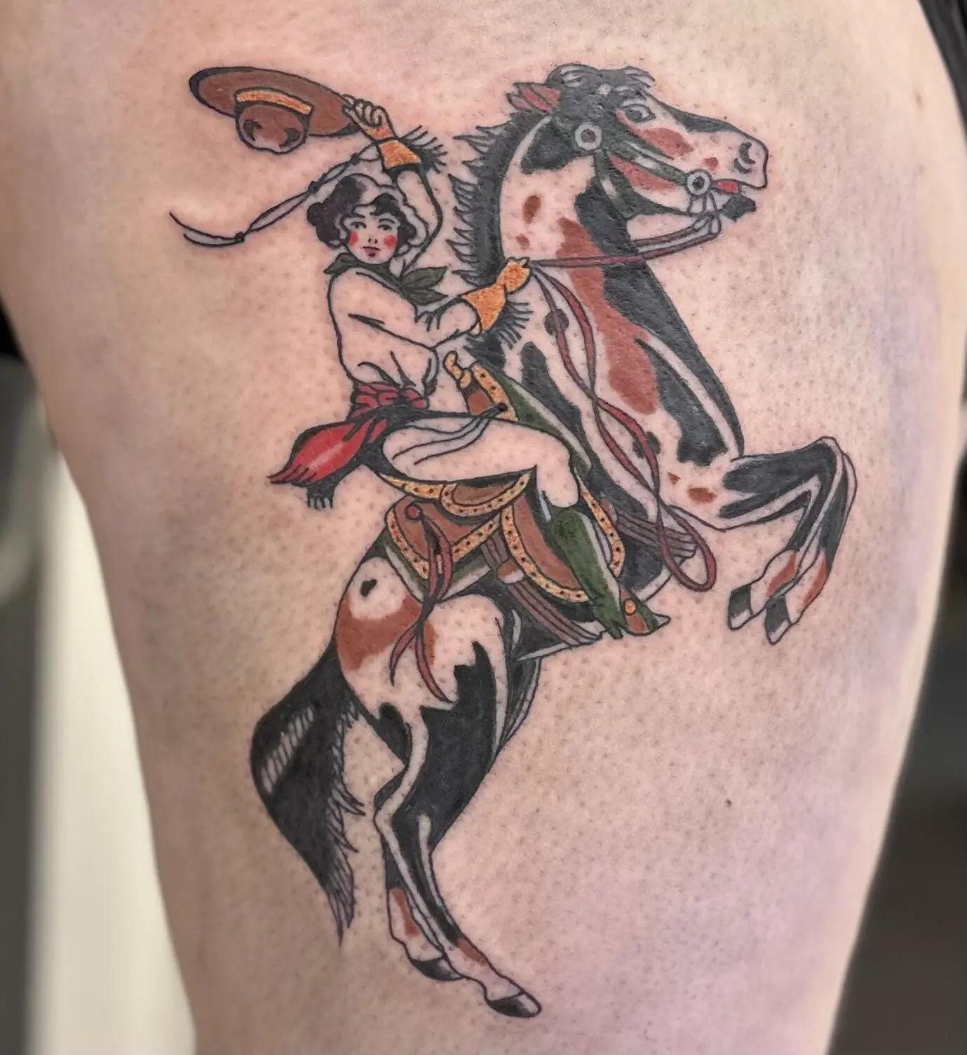 American traditional thigh tattoo of a cowgirl riding a rearing pinto horse with lasso and sombrero, by Carly