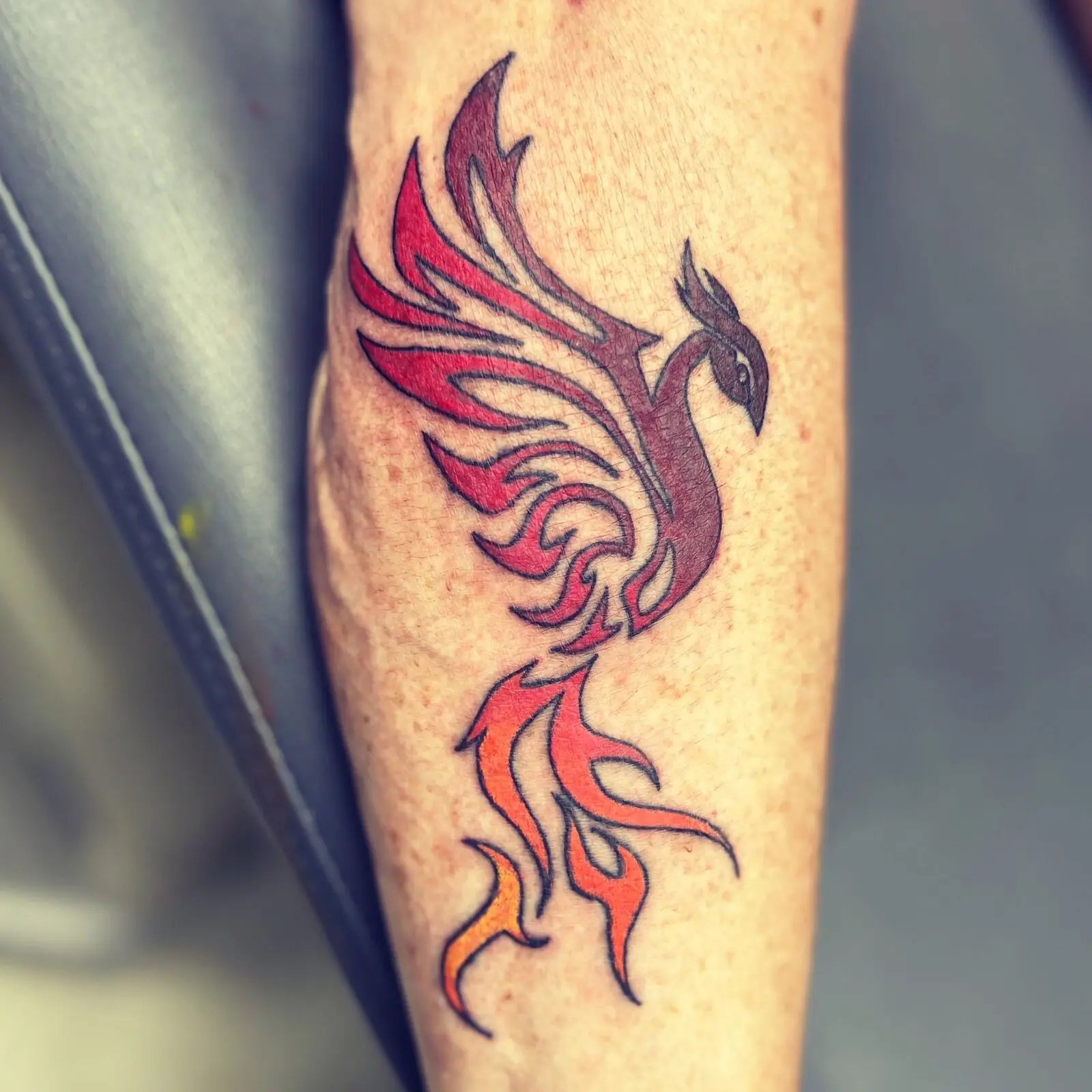 Tribal-style phoenix tattoo rising with red and orange flame feathers on the lower leg